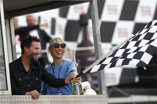 Keanu Reeves and Alexandra Grant waving the checkered flag at the German Grand Prix.