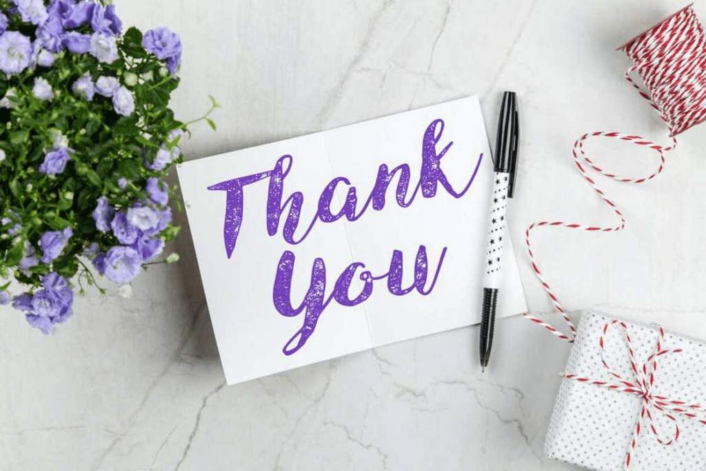 A handwritten thank you card next to a gift and flowers.